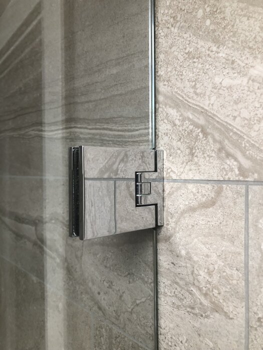 Dörrgångjärn i metall monterat på beige kakelvägg.