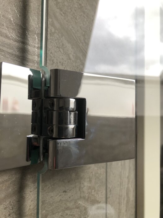 Närbild av ett metallgångjärn fäst vid en glasdörr mot en stenvägg, som ska lyftas ner utan att skadas.