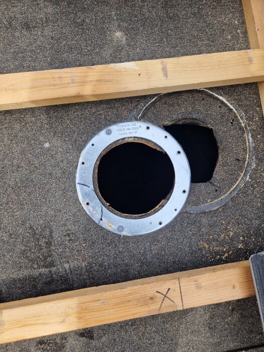 Närbild av tak med urtag för flexrör, metallkrage monterad över hål. Träribba synlig över kanten.