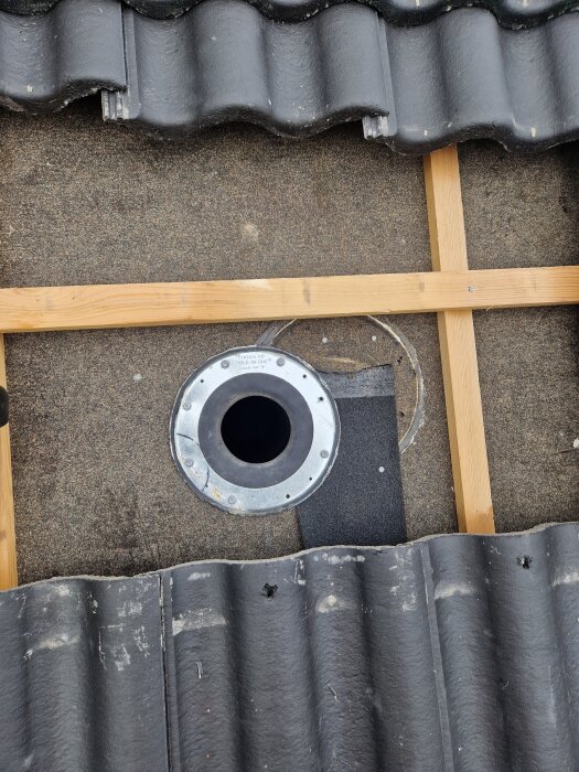 Tak med öppning för flexrör, omgiven av svarta takpannor, synlig metall- och gummikrage samt träreglar.