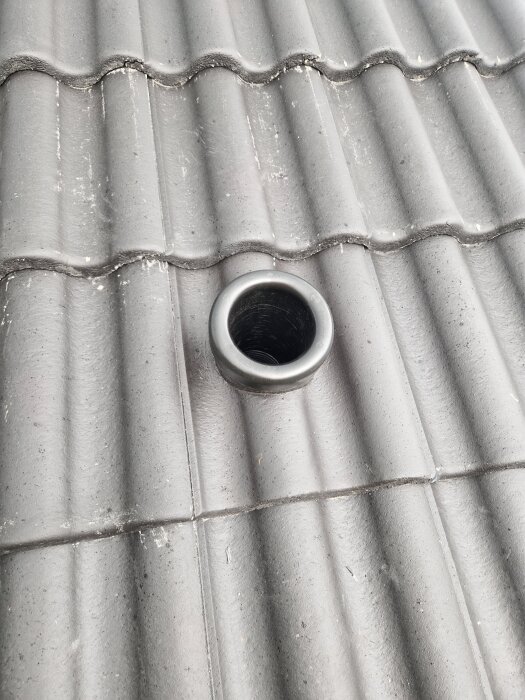 Tak med grå takpannor och ett installerat rör med metallkrage som sticker upp mellan pannorna.