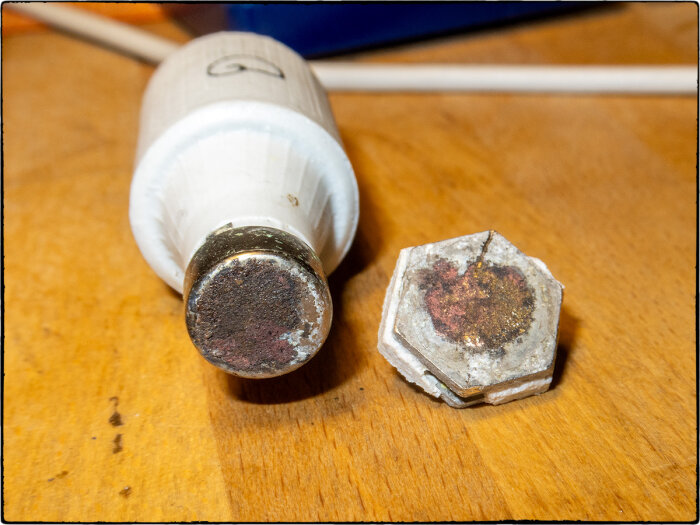 Skadad el-säkring med saknad porslinsdel och märken på metallbasen, placerad på en träyta.