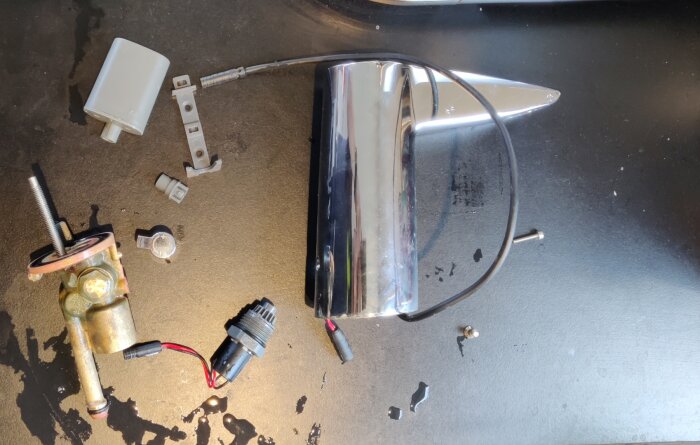 Delar av en isärplockad Oras IR-vattenkran ligger på en arbetsyta, tillsammans med en handlampa på batteri.