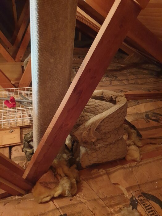 Eternitrör och isolering på vind i 70-talshus med träbalkar och nät på golvet.