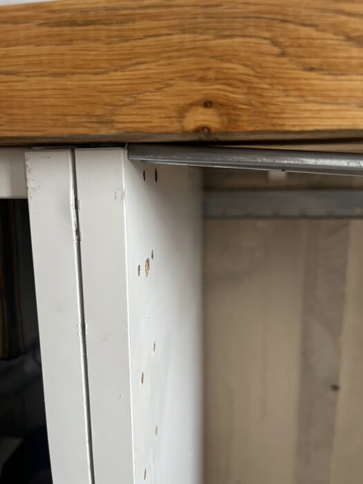 Vänster skåpstomme utan skruvar med en stålskiva överst syns inuti ett skåp med träkant upptill.