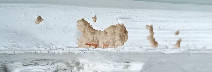 Närbild av ett fönster där vissa delar av kittet är borttaget, med synligt trä under och ojämna kanter.