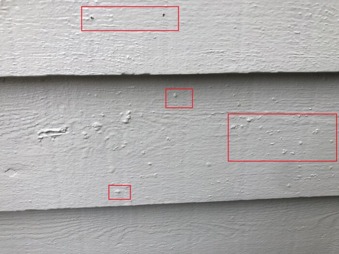 Närbild av villafasad med rödmarkerade områden som visar rinnmärken och infärgade björkfrön på de liggande brädorna efter målning.