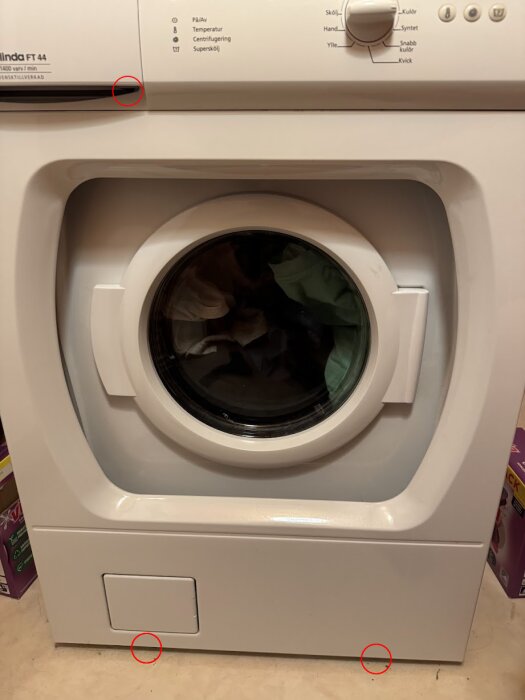 Framsida av en tvättmaskin med detaljer markerade, inklusive platsen för tre Torx-skruvar vid doseringsluckan och nödöppnaren vid rensluckan.