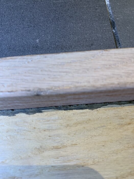 Golvtröskel vid badrum med synliga tecken på fukt och vita fläckar på golv och vägg.