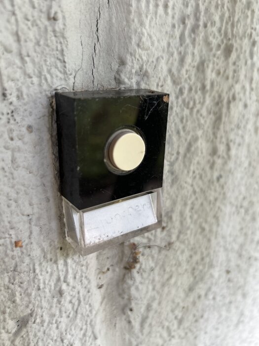 Rund knapp av en ringklocka installerad på en vit, grov vägg.