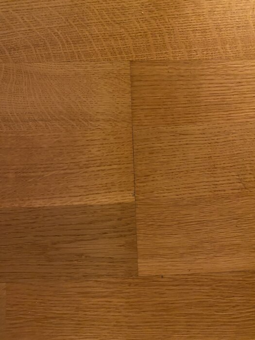 Närbild av trägolv med synliga springor mellan plankorna där det är mörkt, potentiellt tecken på fukt- eller mögelskada.