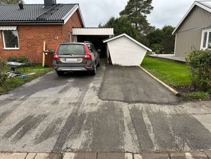 Grusad uppfart framför en röd tegelvilla med en parkerad bil och en vit bod. Nygrusat område bredvid den asfalterade uppfarten.