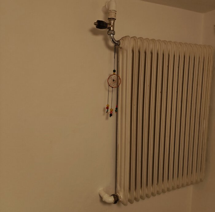 Gammal vit radiator med metallrör och drömfångare hängande på.