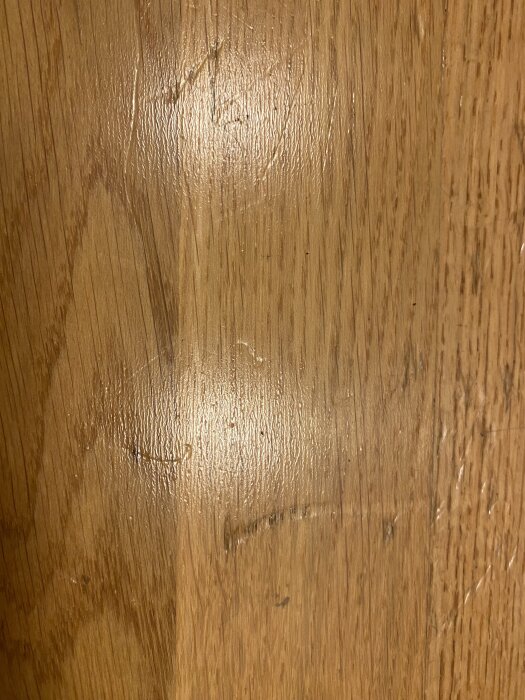 Slitaget och glansen på golvets yta syns tydligt, med djupa hack som får det att se plastigt ut. Möjlig fråga om det är parkettgolv.