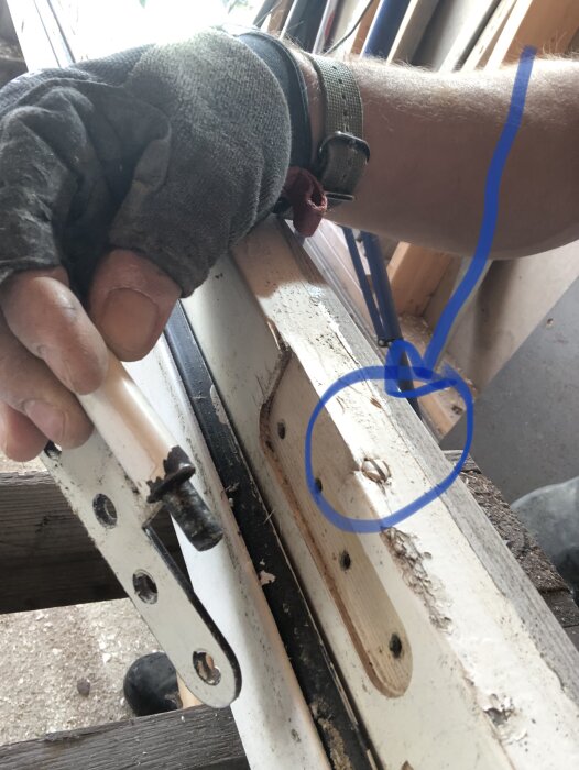 En hand håller i en dörrkarm med tre gångjärn, där en skruv i karmen är inringad i blått. Skruvens funktion ifrågasätts i texten.