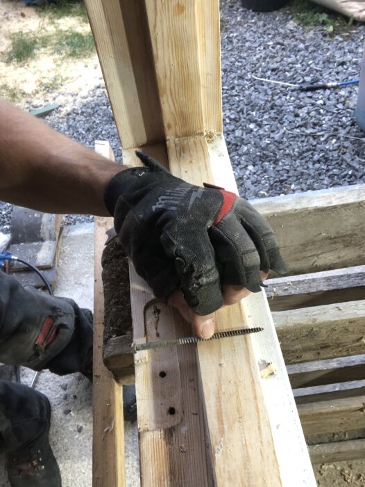 Person med arbetshandske håller en lång skruv vid en äldre träkarm under renovering av en ytterdörr.