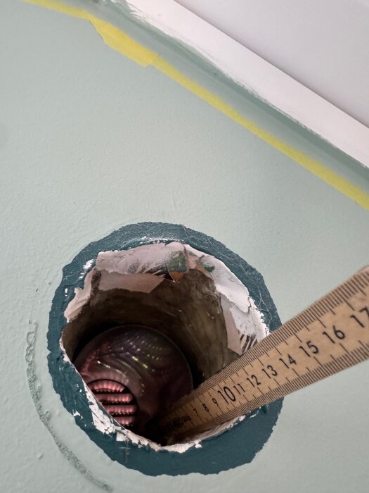 Hål i grön vägg med blottlagd isolering visas, med en linjal på 16 cm instoppad i hålet.