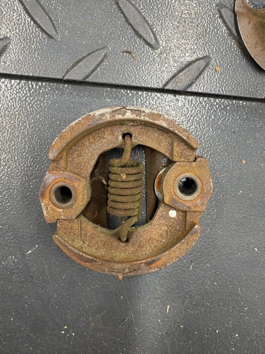 Sliten röjsågskoppling med ojämna slitytor och rostig yta på ett verkstadsgolv.