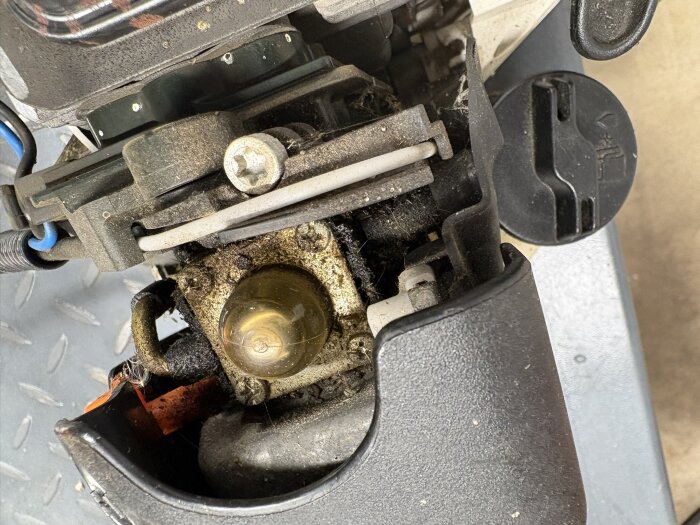 Röjsågsmotor med synliga koppling och bränslekopplingar, delvis demonterad för service. Kopplingen ser sliten ut och area kring bensinlocket är smutsig.