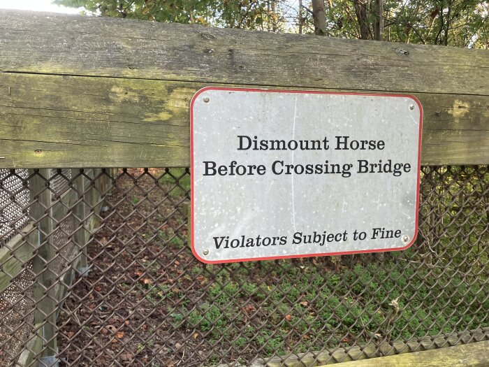 Skylt på trästaket som instruerar att gå av hästen innan man korsar bron.