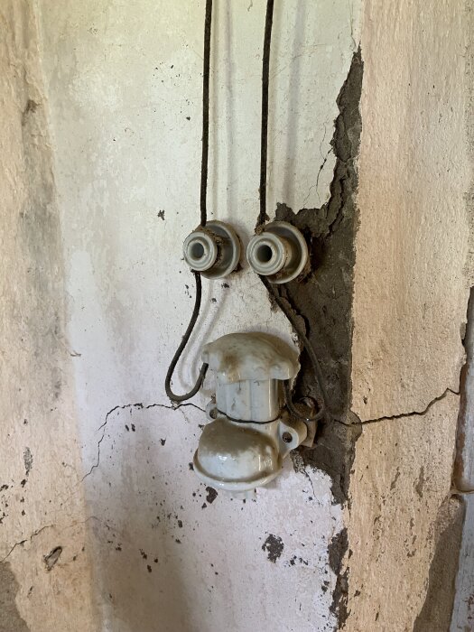 Gammal strömbrytare monterad på sprucken, vitmålad vägg.