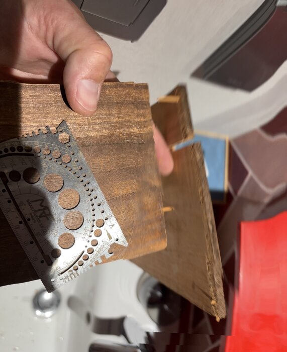 En person håller en träbräda och en silverfärgad mätsticka, arbete med träbearbetning i ett badrum med en handfat i bakgrunden.