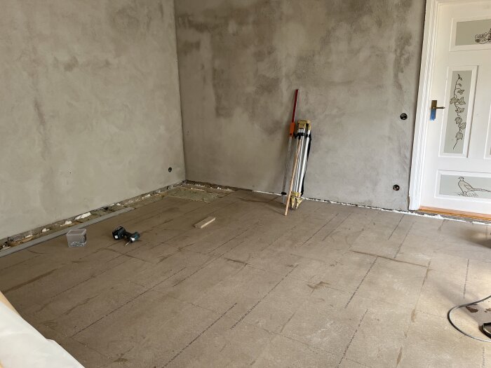 Renoverat rum med nyputsade väggar och golvspån redo för golvläggning. Verktyg och material syns på golvet.