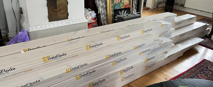 Golvmaterial från DalaFloda staplade i ett rum med en kakelugn och tavlor i bakgrunden, redo att installeras.
