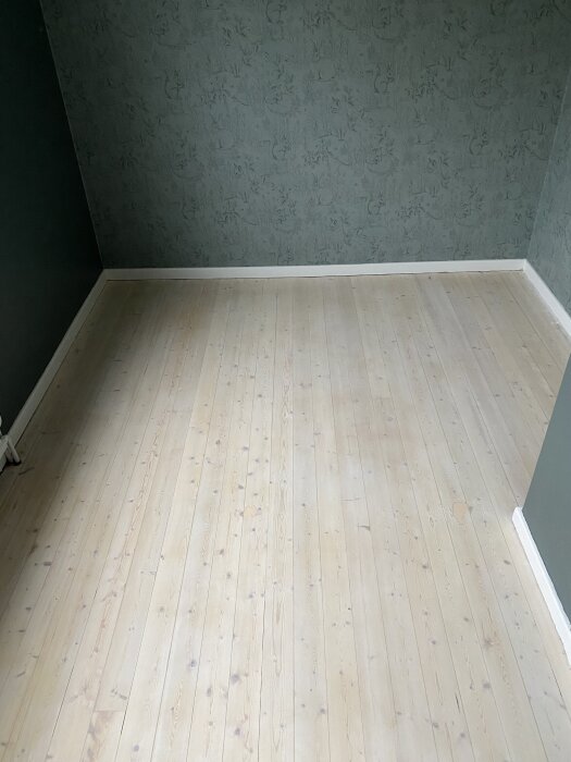 Nybehandlat trägolv i ett rum med gröna väggar och vit golvlist.