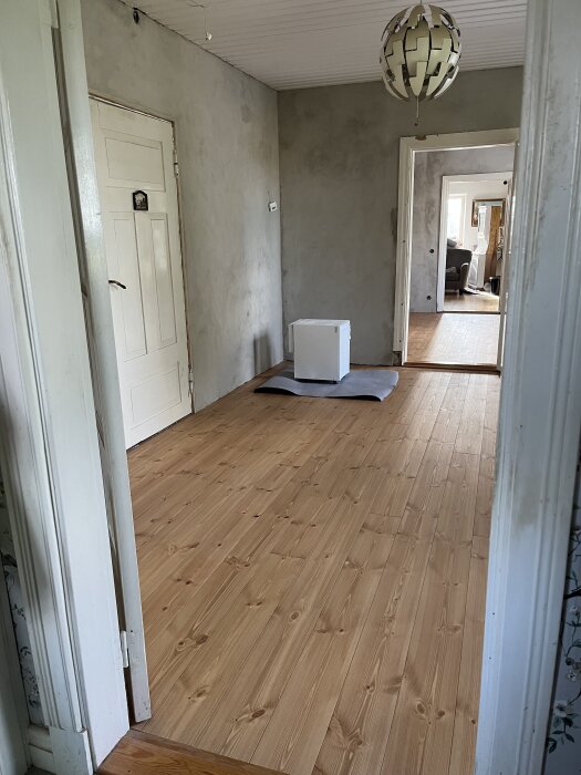 Nytt trägolv i renoverat rum med grå putsade väggar och en avfuktare stående på golvet. Ljuskrona hänger i taket.