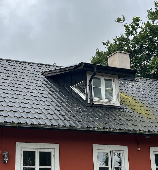 Tak med svart takpanna, röd vägg, takkupor och nymålad skorsten, omgiven av träd.