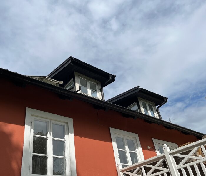 Takkupor på rött hus med vita fönsterkarmar och nymålade putslager, del av renovering för att förbättra täthet och hållbarhet.