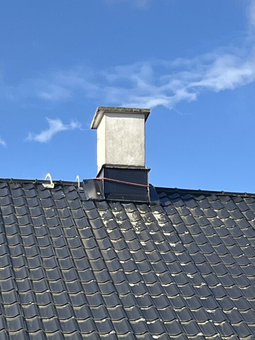 Nyputsad skorsten på ett tak med svarta takpannor, under klarblå himmel.