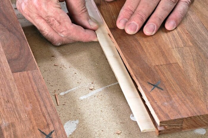Person monterar parkettgolv med not och fjäder; fjädern är en ljus remsa, placeras i ett spår på golvplankan.