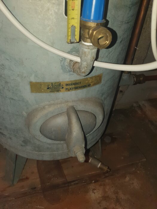 Hydrofor med plaströrsanslutning, ventil och etikett från Värslund Verkstad. Rustig yta och placering på trägolv i källare.