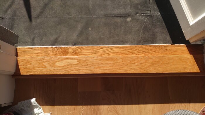 Renoverad balkongtröskel i trä, slipad och behandlad med hårdvaxolja. Mörka spår delvis borttagna, omgiven av skugga.