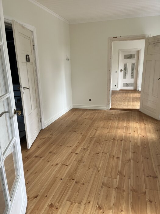 Ljust rum med nymålade vita väggar, ljusa trägolv och öppna dörrar som leder till fler rum; uppdateringar inkluderar ny färg och golvpappens borttagning.