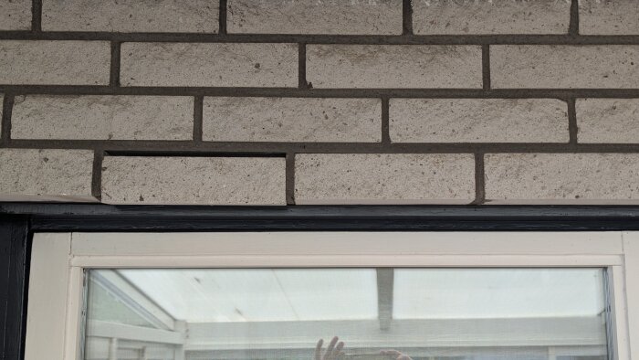 Lösa tegelstenar ovanför ett fönster, en sten borttagen.