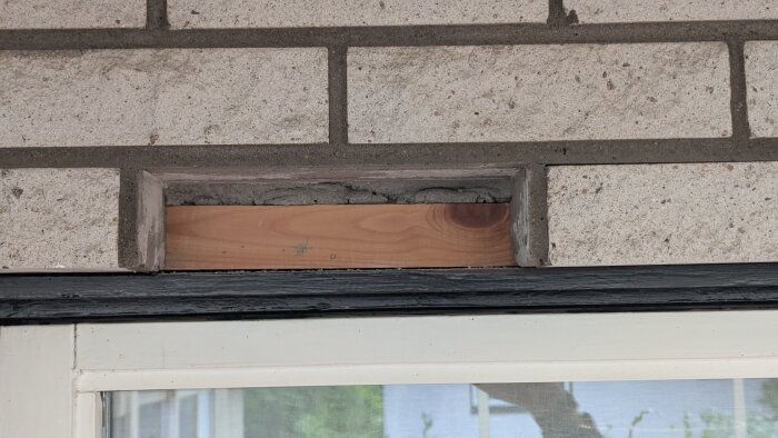 Löst tegel ovanför ett fönster med synlig träregel bakom.