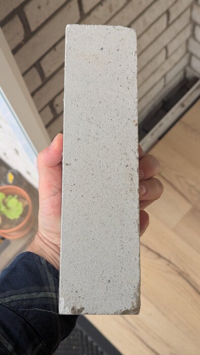 En person håller en lång, rektangulär stenplatta, troligtvis en lös del från ett hus, med en tegelvägg i bakgrunden.