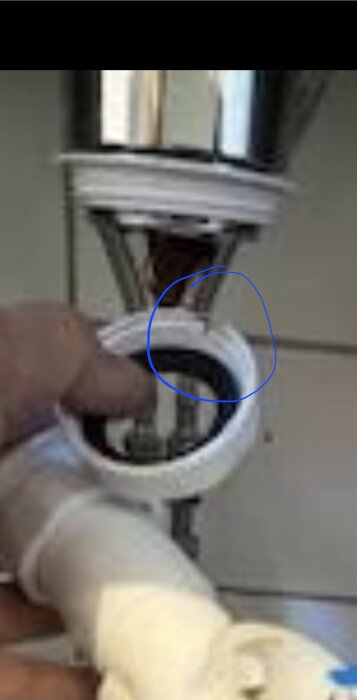 En hand håller ett rör vid en köksvask, med fokus på en gummiring i röret. En blå cirkel markerar området.