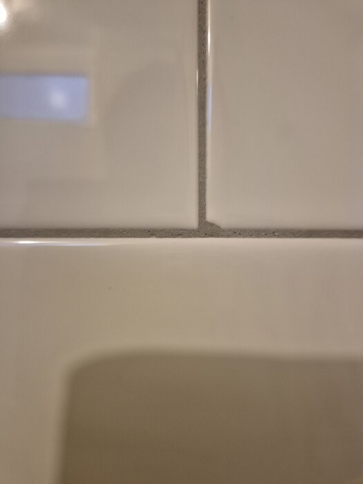 Vita kakelplattor med ojämn fogning och intryckta kanter, fokus på hörn och list runt fönster.