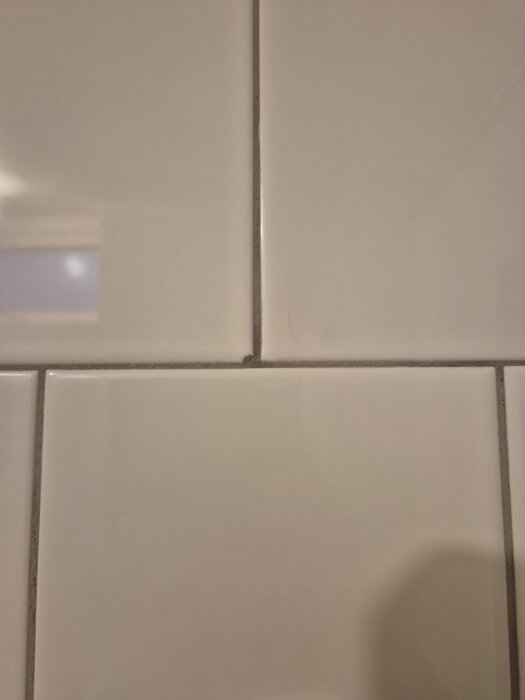 Vita kakelplattor med en platta som ser intryckt ut; hörn saknas och ojämn list runt fönster enligt beskrivning.