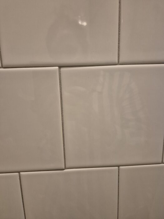 Vita kakelplattor på en vägg där vissa hörn saknas och en platta ser intryckt ut.