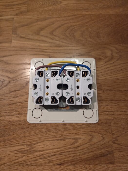 Två vita kopplingsklämmor med bruna, blå och gula kablar fästa på en träliknande yta.