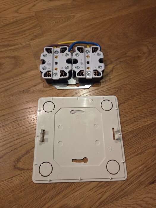 Två elektriska kopplingsdosor på trägolv med plastlock bredvid, kablar synliga.