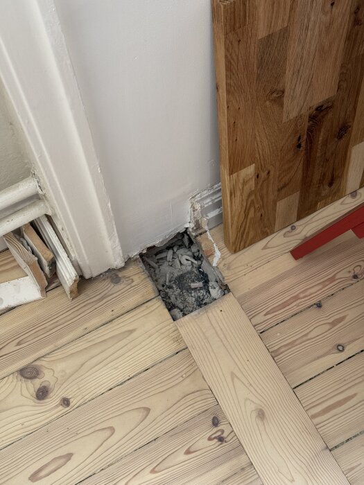 Golv i furu med synligt hål vid vägg efter rivning, och en ny bräda lagd tvärs över det ursprungliga golvet.