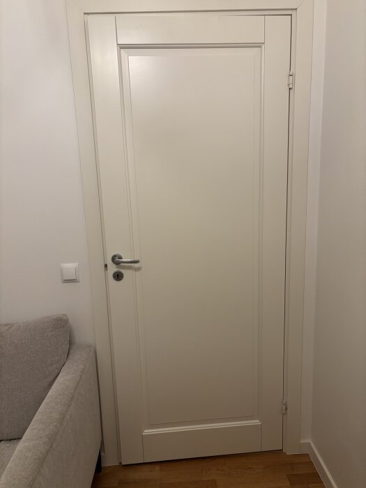 Vit innerdörr med dörrhandtag och synligt mellanrum mellan dörr och karm, fotograferad i en bostadsrätt från 2017.