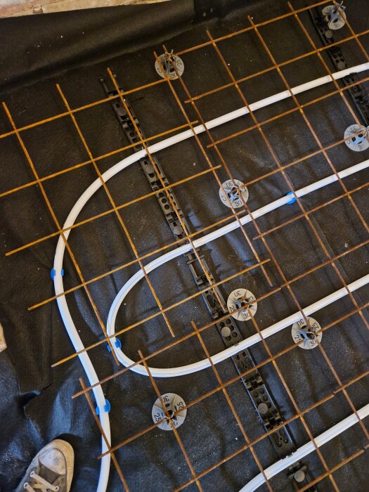 Armeringsnät och golvvärmeslang över betonggrund, monterade på avståndshållare, med fokus på nätets positionering vid skarvar.