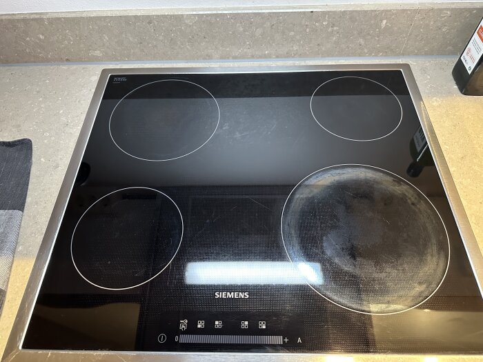 Närbild på en spishäll med en flammig, rengjord yta och synliga märken på den nedre högra plattan.